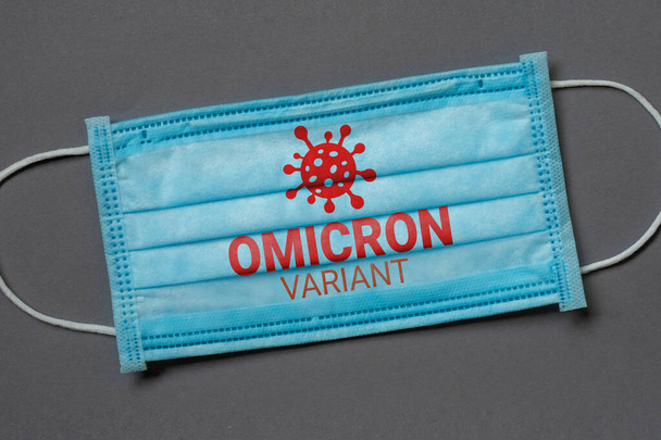 Een blauw medisch gezichtsmasker ligt op een donkergrijze achtergrond met de inscriptie omicron variant, coronavirus concept - Foto, afbeelding
