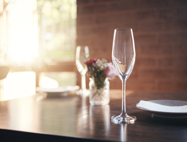 Üres pohár az asztalon bor, pezsgő vagy alkohol vacsorához romantikus étteremben, otthon vagy étteremben. Luxus, ebéd vagy vacsora kristály borospohárral, tányérral és virággal recepcióhoz, banketthez vagy ételhez. - Fotó, kép