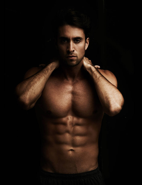 Ripped abs. Portrait of a handsome young man showing off his six pack - Isolated on black - Photo, image