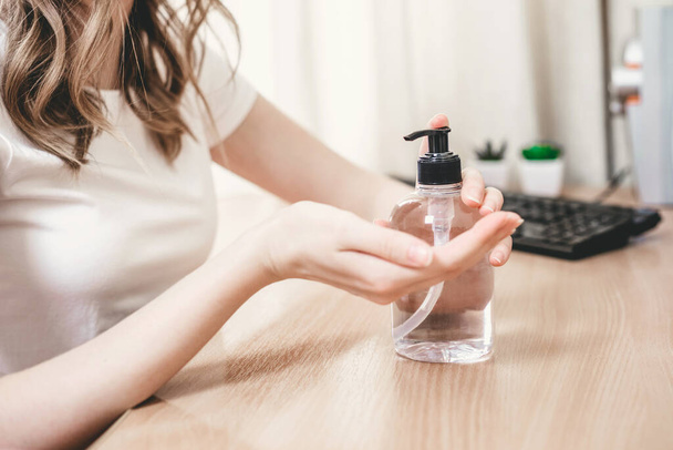 Meisje wast haar handen met gel antiseptisch en gebruik een antibacteriële alcohol voor de hand hygiëne tegen coronovirus bacteriën, pandemie, quarantaine. Een fles ontsmettingsmiddel op tafel. - Foto, afbeelding