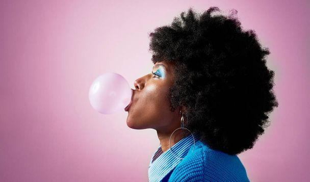 Gomme à bulles, cheveux afro et femme noire sur fond de studio rose avec coiffure tendance mode, cool ou jamaïcaine. Modèle profil, tête ou beauté avec gomme à mâcher, maquillage et attitude audacieuse ou amusante. - Photo, image