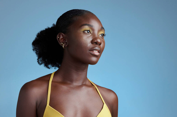 Zwarte vrouw schoonheid en gele make-up cosmetica model voor oogproduct in blauwe achtergrond studio mockup. Nigeria Afrikaans jong meisje poseren voor natuurlijke haarverzorging, gezonde huidverzorging en afro empowerment. - Foto, afbeelding