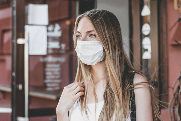 Young woman wears a medical mask on building facade background, quarantine, coronavirus - Фото, изображение
