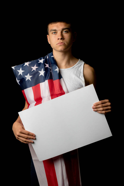 A portrait of a nineteen year old teen boy on a black background with an American Flag and white board - Zdjęcie, obraz
