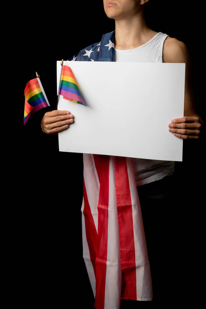 A portrait of a nineteen year old teen boy on a black background with an American Flag and white board and Pride Flags - Фото, изображение