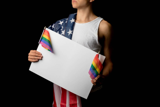 A portrait of a nineteen year old teen boy on a black background with an American Flag and white board and Pride Flags - Foto, Imagem