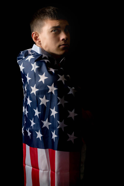 A portrait of a nineteen year old teen boy on a black background with an American Flag from behind - Foto, imagen