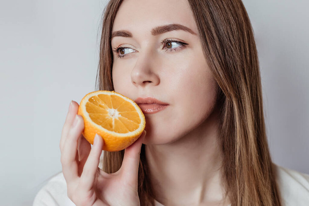 Utrata węchu. Close up portret młodej kobiety rasy kaukaskiej trzymając pomarańczę w pobliżu jej nosa odizolowane na białym tle w studio - Zdjęcie, obraz