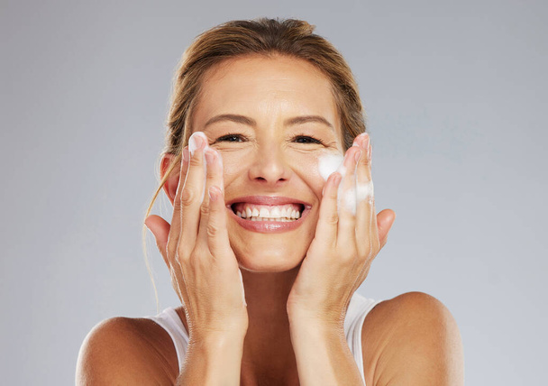 Skincare, clean and face portrait of a woman washing her skin with beauty treatment in a studio. Happy, smile and healthy mature lady with health, hygiene and self care lifestyle doing facial routine. - Photo, Image