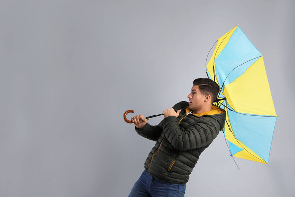 Emotional man with umbrella caught in gust of wind on grey background - Fotografie, Obrázek