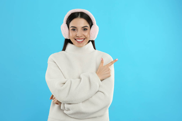 Beautiful young woman wearing earmuffs on light blue background. Space for text - Photo, image