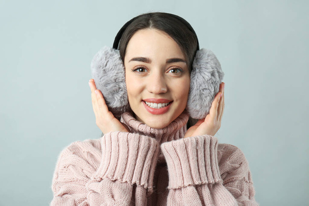 Beautiful young woman wearing earmuffs on light grey background - Foto, afbeelding