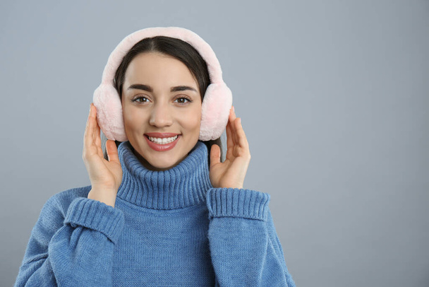 Beautiful young woman wearing earmuffs on light grey background. Space for text - Φωτογραφία, εικόνα