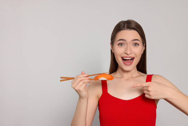 Emotional young woman holding sushi with chopsticks on light background. Space for text - 写真・画像