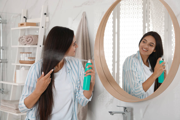 Woman applying dry shampoo onto her hair near mirror in bathroom - 写真・画像
