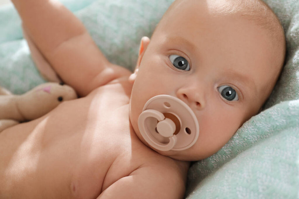 Cute little baby with pacifier lying on soft blanket, closeup - Photo, image