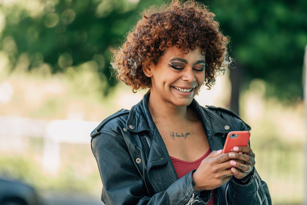 чернокожая девушка на улице, глядя на мобильный телефон или смартфон - Фото, изображение
