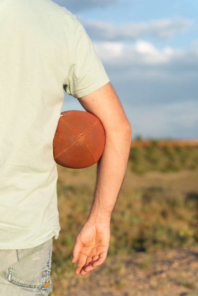 Visão traseira de um homem irreconhecível segurando uma bola de rugby com o braço. - Foto, Imagem