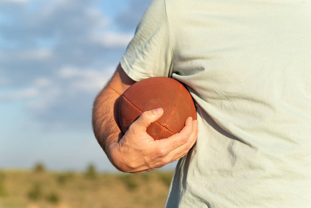 Vista horizontal de una mano masculina sosteniendo una pelota de rugby. - Foto, imagen