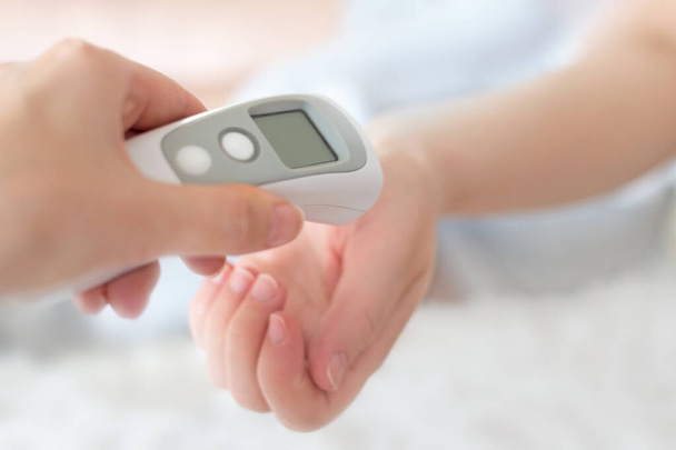 La mano di una donna applica un termometro a infrarossi per misurare la temperatura corporea. Febbre alta con influenza e raffreddore. Prevenzione del coronavirus. Misurazione della temperatura corporea a casa. Assistenza sanitaria. Infezione virale - Foto, immagini
