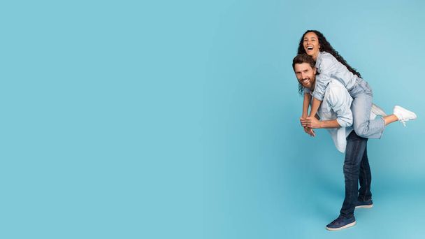 Satisfied young european guy hold on back arabic woman, have fun together, enjoy spare time, isolated on blue background, panorama, studio. Family relationship, love, good offer, ad, mockup and sale - Fotografie, Obrázek