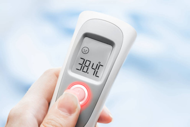 Hand holding ir thermometer with normal temperature. close up. Infrared temperature measuring device. Healthcare home action. Non-contact thermometer - Photo, Image