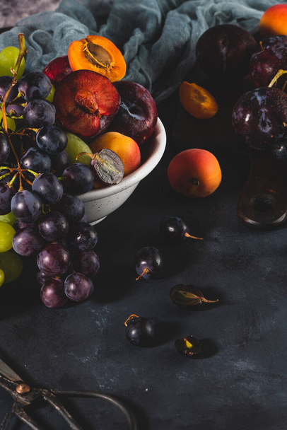 新鮮な果物を水滴で洗います。鮮やかなキールックが新鮮さを伝えます。暗色の背景に新鮮なブドウ、アプリコット、梅の様々な。ビタミンの果実源 - 写真・画像