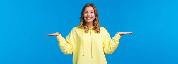 Carefree happy smiling woman weighing something in arms, as if holding two products, look camera suggest make choice, deciding between variants, stand blue background. - Photo, Image