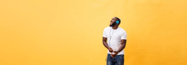 Volledige lengte portret van een kers jonge Afro-Amerikaanse man, luisteren naar muziek met een koptelefoon en geïsoleerde dansen op gele achtergrond. - Foto, afbeelding