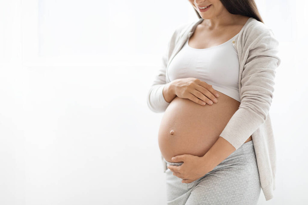 Cropped shot of pregnant woman in homewear touching her big belly, unrecognizable lady expectant waiting for baby, white studio background, panorama with copy space, closeup - Foto, Bild