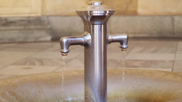 Grifo suministra agua de curación de fuentes en la cuenca de piedra profunda. Alto grifo de metal da agua de manantial medicinal para el turista al gusto en la ciudad balneario - Imágenes, Vídeo
