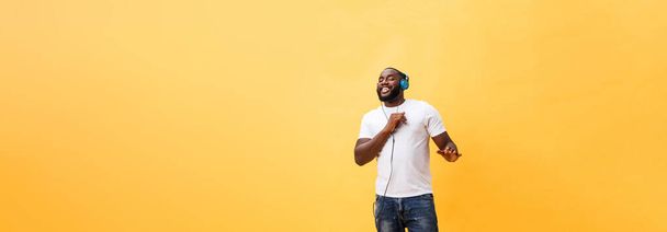 Po celé délce portrét cherry mladé afroamerické muže poslouchá hudbu se sluchátky a tanec izolované na žlutém pozadí. - Fotografie, Obrázek