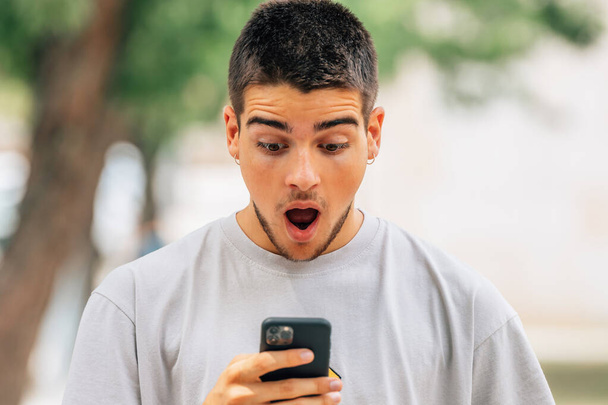 järkyttynyt nuori mies kadulla katsomassa matkapuhelinta tai älypuhelinta - Valokuva, kuva