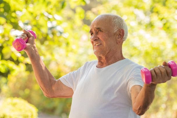 senior man doet sport of lichaamsbeweging buiten met halters - Foto, afbeelding