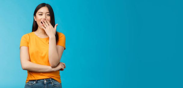 Sleepy cute asian brunette yawning waiting for cup coffee morning standing office smiling upbeat, cover opened mouth waking up feel energized, stand blue background. Copy space - Photo, Image