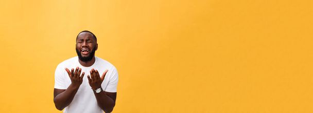 Studio portret van jonge African American man in wit overhemd, bedrijf handen in gebed, kijken naar de camera met doordachte sceptisch uitdrukking op zijn gezicht, vermoeden van iets. Lichaamstaal - Foto, afbeelding