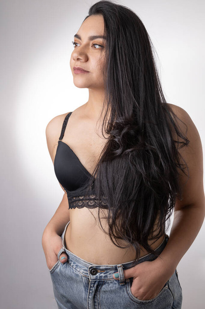 retrato de estudio foto de una joven latina con el pelo largo y la piel morena, lleva un sujetador y jeans, moda casual y sensual, belleza natural - Foto, Imagen