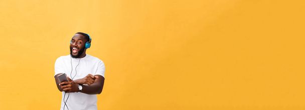 Hombre afroamericano con auriculares escuchar y bailar con música. Aislado sobre fondo amarillo
. - Foto, imagen