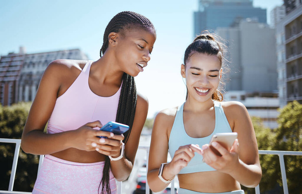 Friends, phone and laughing during exercise for social media, blog or meme while in city together. Women, smartphone and smile with diversity during training, workout or run in Los Angeles in summer. - Photo, Image