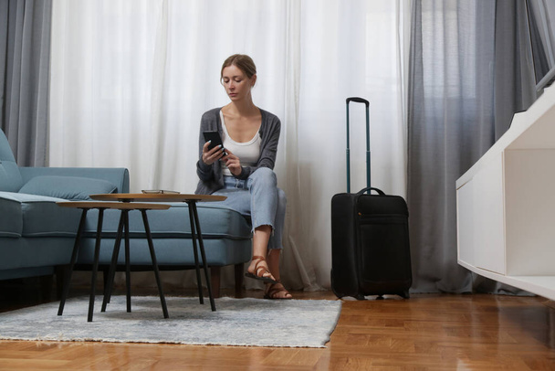 Nuori nainen matkailija älypuhelimen ja matkatavaroiden kanssa hotellihuoneessa - Valokuva, kuva