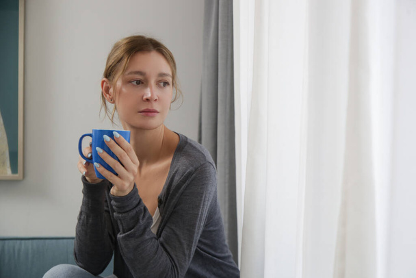 Zrelaksowana młoda kobieta ciesząca się filiżanką kawy w salonie, relaksujący dzień samoopieki w domu koncepcja. - Zdjęcie, obraz