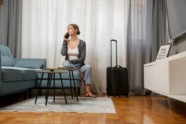 Jeune voyageuse avec smartphone et bagages dans la chambre d'hôtel - Photo, image