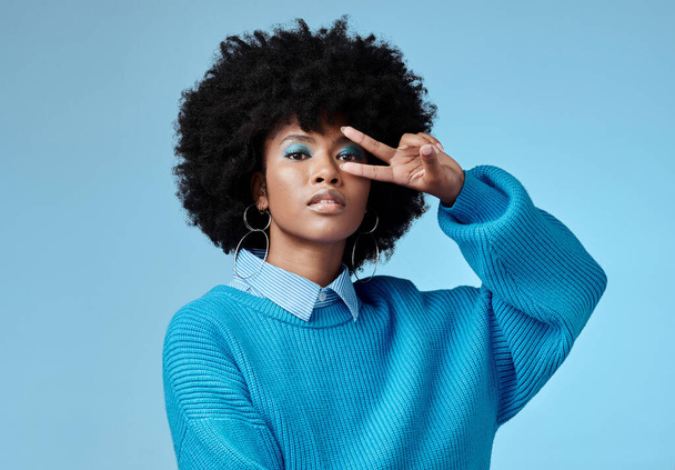 Portrait, young and black woman shows peace, sign and with blue studio background, afro and stylish look. Girl, happy lady and female with confident, relax and casual or funky outfit for fun day - 写真・画像