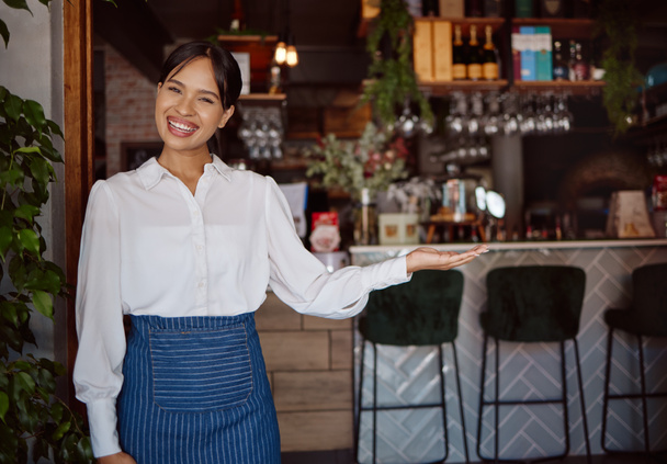 Welcome, restaurant waiter and business owner giving service with a smile at a coffee shop. Portrait of a black woman working as a waitress at a cafe, coffee shop or small business for fine dining. - 写真・画像