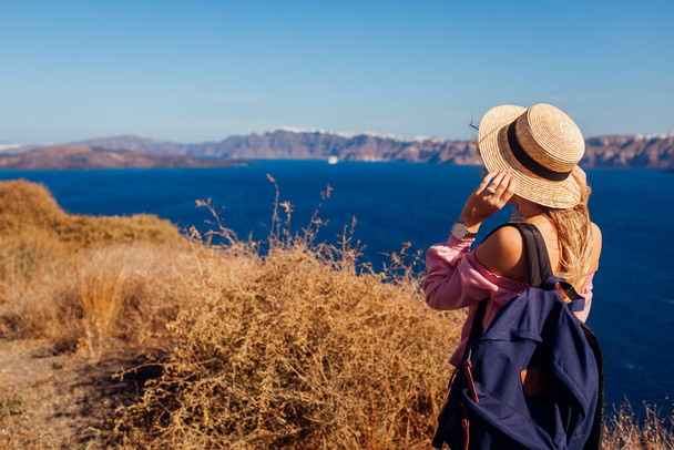 Вид сзади на женщину, прогуливающуюся по греческому острову Санторини, наслаждающуюся морским пейзажем. Турист с рюкзаком смотрит на Кальдеру. Космос - Фото, изображение