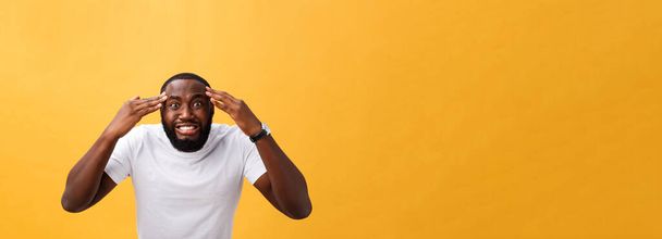 Portrait of african american man with hands raised in shock and disbelief. Isolated over yellow background - 写真・画像