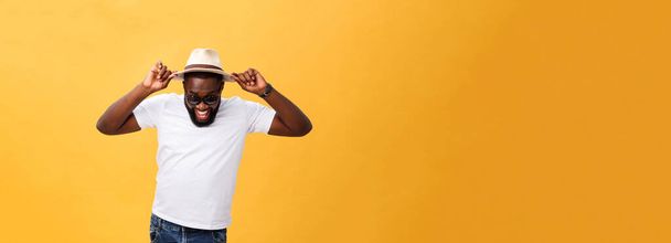 Close up portrait of a young man laughing with hands holding hat isolate over yellow background. - Fotó, kép