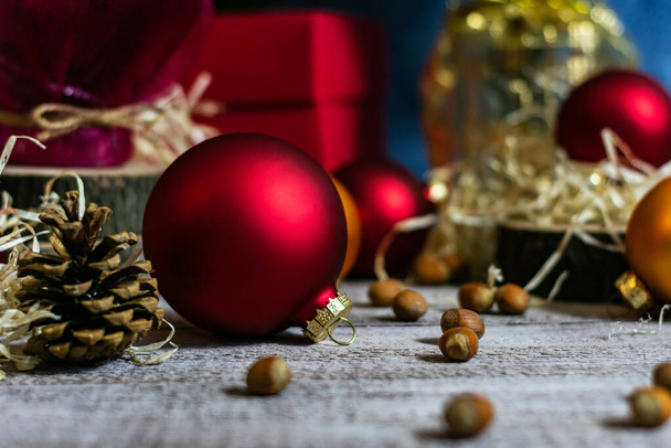 Kırmızı topların yakın plan fotoğrafı, koniler ve fındıklar arasında defocus içinde ahşap bir masa üzerindeki bir Noel ağacını süslemek için. - Fotoğraf, Görsel