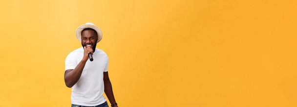 jonge knappe Afro-Amerikaanse jongen emotionele zingen met microfoon geïsoleerd op gele achtergrond, in beweging gebaren. - Foto, afbeelding