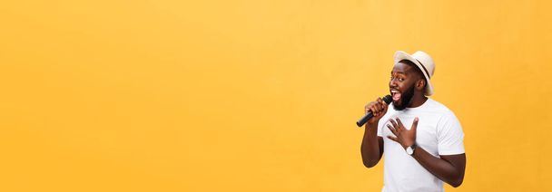 młody przystojny chłopak african american śpiewając emocjonalne z mikrofonem na białym tle na żółtym tle, w ruchu gestem. - Zdjęcie, obraz